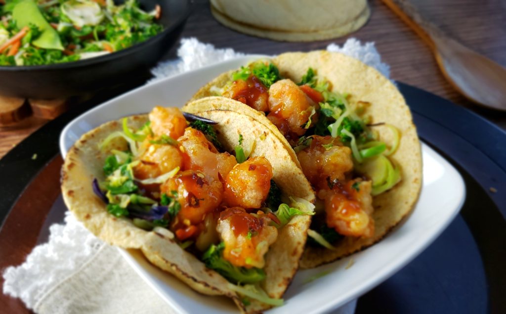 Sesame Ginger Shrimp Tacos with Stir Fry Veggies is an under-30 minute meal that is made healthier by oven baking the shrimp rather than frying -- still crunch and delicious with a gluten-free breading! Stir fry vegetables add colorful nutrition and can be adjusted to your preferences.